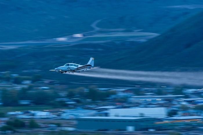 This photo shows a side view of a plane spraying trees in Kamloops at dawn. 