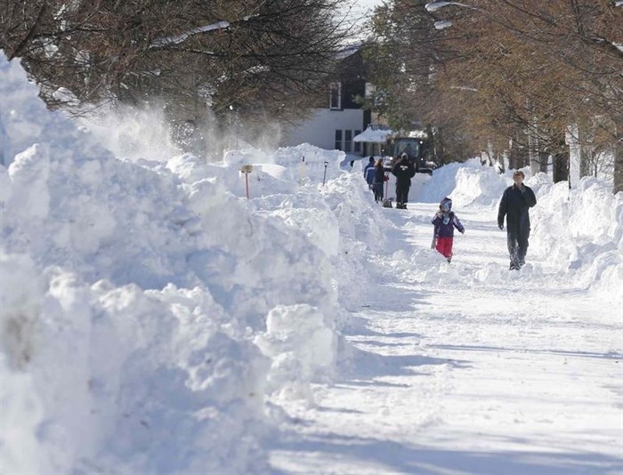 People walk along a snow-covered street in the south Buffalo area on Friday, Nov. 21, 2014, in Buffalo, N.Y.