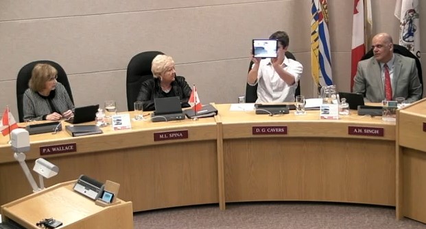 Coun. Donovan Cavers holds up a picture of a sign at Thompson Rivers University and asks council who wouldn't recognize a red octagonal sign in any language.