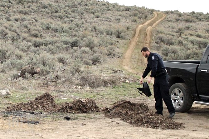 Conservation Officer Rob Armstrong checks the contents of a laptop bag dumped among a pile of garbage.