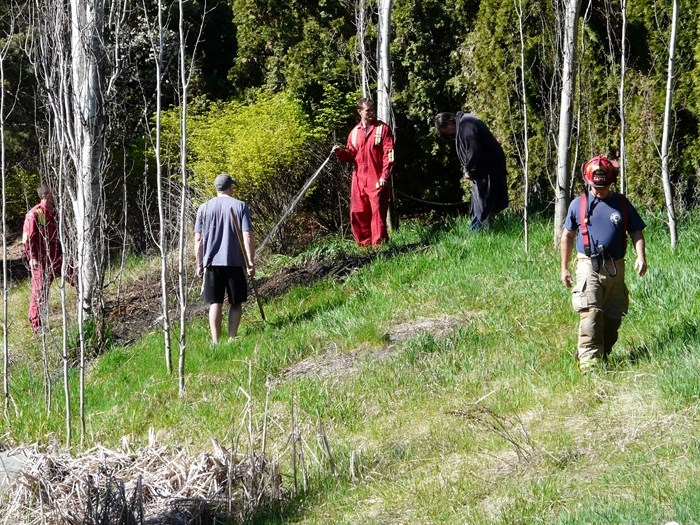 A Kelowna firefighter mops up a small grass fire with a garden hose in Brant's Creek Linear Park Sunday morning, April 19, 2015, while residents, who helped put out the fire, look on.