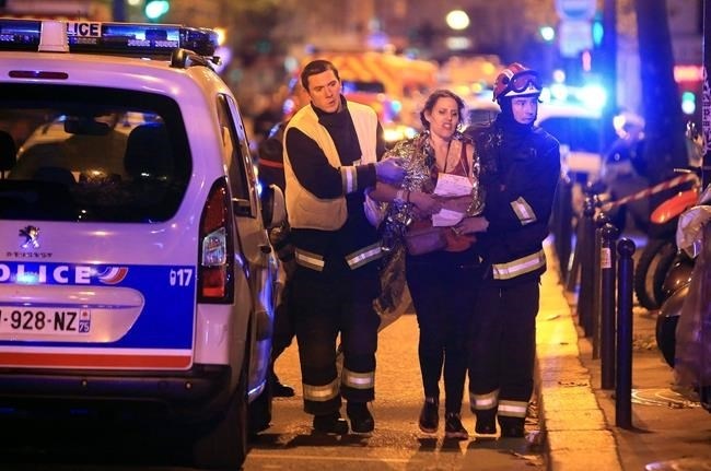 Rescue workers help a woman after a shooting, outside the Bataclan theater in Paris, Friday Nov. 13, 2015.