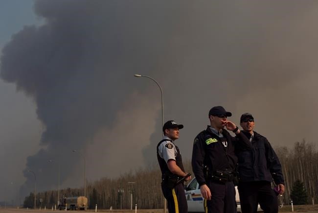 Police man a roadblock as smoke billows in the background near a wildfire in Fort McMurray, Alta., on Friday, May 6, 2016. 