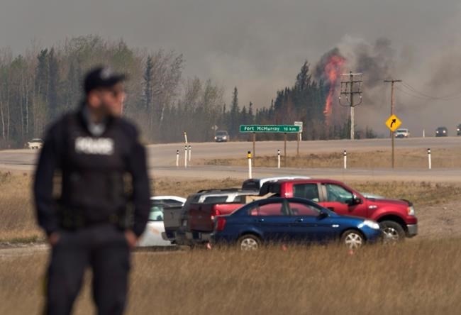 A police officer stands at a roadblock as a fire flares up near Fort McMurray, Alta., on Friday, May 6, 2016.