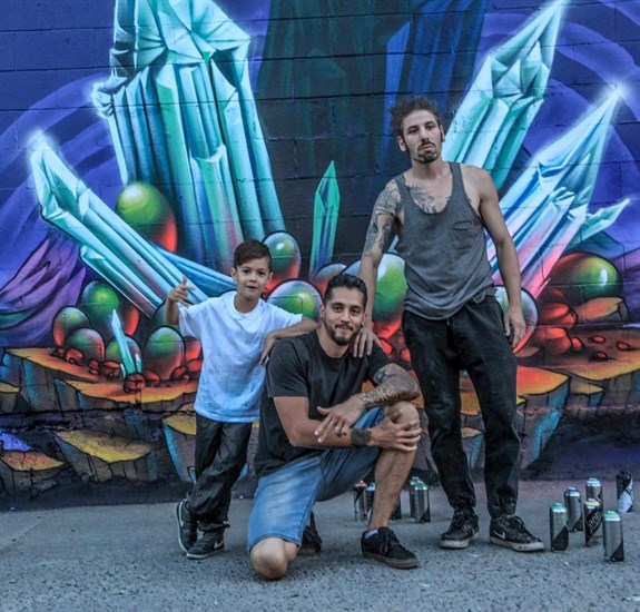 “Frisco” Ugarte (centre), Karram Amro, along Frisco's son Tao, the organizers of the Fresh Coast Championship in front of the new mural on the wall of Hotel Zed that they also helped organize. 