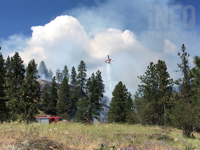 A helicopter dumps a load of water on a grass fire burning near Westside Road in Traders Cove north of West Kelowna, Tuesday, June 13, 2017.