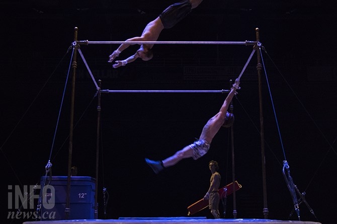 Two acrobats practice stunts on the set of one of the last scenes in the production. An onlooker carries a crash mat that he will drape over one of the poles, creating a new obstacle.