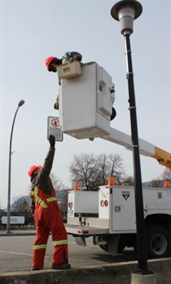 City of Penticton workers remove signs from street lights alongside the Okanagan Lake waterfront today. These lights will be replaced entirely with LED versions.