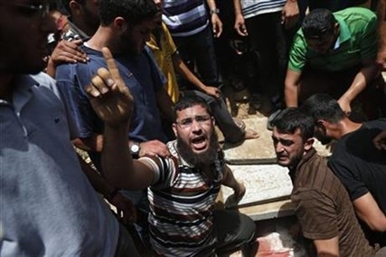 A Palestinian mourner chants slogans on the grave of a member of the al-Batsh family who were killed in Saturday's Israeli airstrike, during a funeral procession in Gaza City on Sunday, July 13, 2014.
