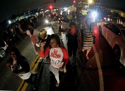Protesters march down the middle of a street, Friday, Aug. 15, 2014, in front of a convenience store that was looted and burned following the shooting death of Michael Brown by police nearly a week ago in Ferguson, Mo.