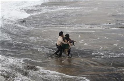 A man, left rescues a woman who fell in water due to strong tidal waves prior to a cyclone on the Bay of Bengal in India, Sunday, Oct. 12, 2014.
