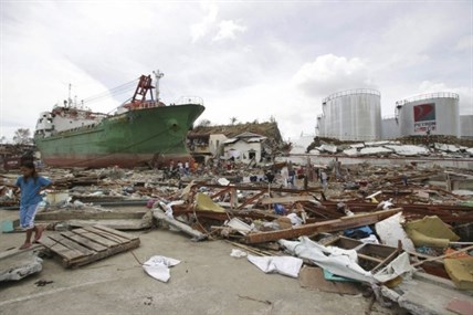 Survivors walk beside a ship that was washed ashore hitting makeshift houses near an oil depot in Tacloban city, Leyte province central Philippines on Monday, Nov. 11, 2013. Authorities said at least 2 million people in 41 provinces had been affected by Friday's typhoon Haiyan and at least 23,000 houses had been damaged or destroyed.