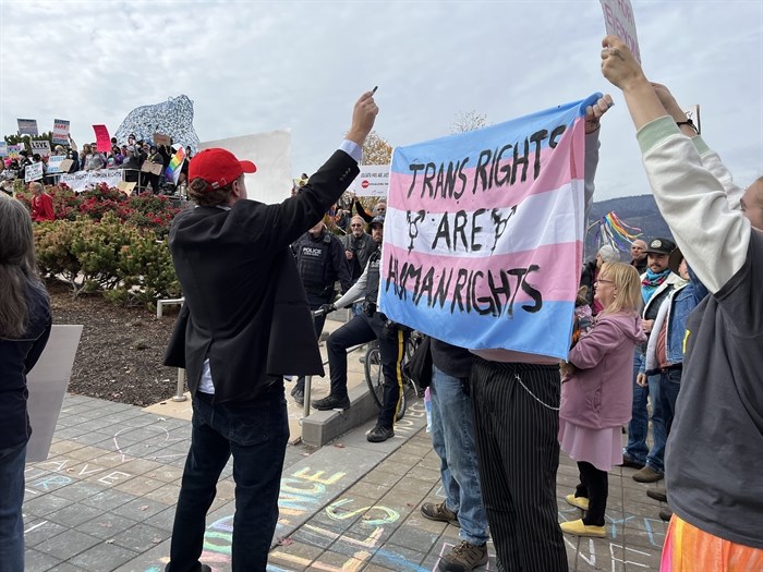 Anti-SOGI protester holding up a sign in front of a trans-rights activist holding up a flag.