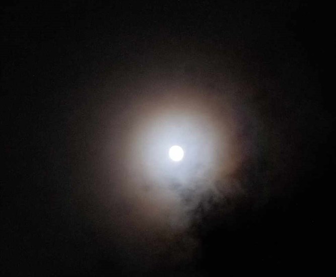December's full Cold moon shining brightly through cloudy skies. 