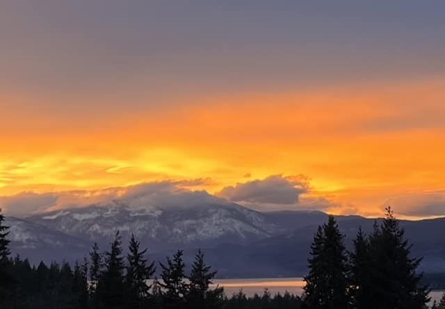 A bright sunset is seen behind snowy mountain tops over Shuswap Lake. 