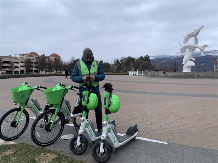 A Lime employee stands in front of some parked e-scooters and e-bikes in downtown Kelowna.