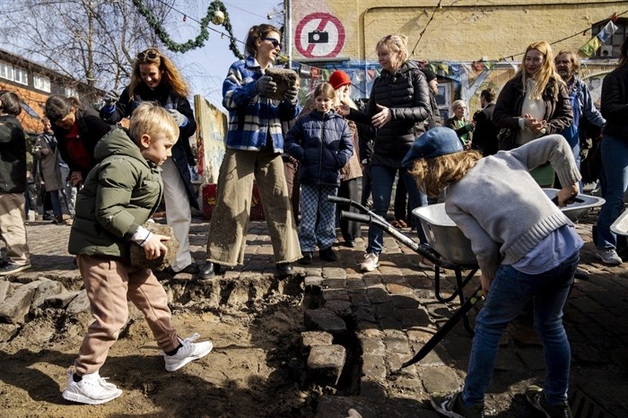 Citizens of the free village Christiania jointly dig up the cobblestones at Pusher Street, in Copenhagen, Denmark, Saturday April 6, 2024. After the cobblestones are removed, new water pipes and a new pavement will be laid on Pusher Street and nearby buildings will be renovated. That is the first step in an overall plan to turn the hippie oasis into an integrated part of the Danish capital area, although “the free state" spirit of creativity and community life is to be maintained. 