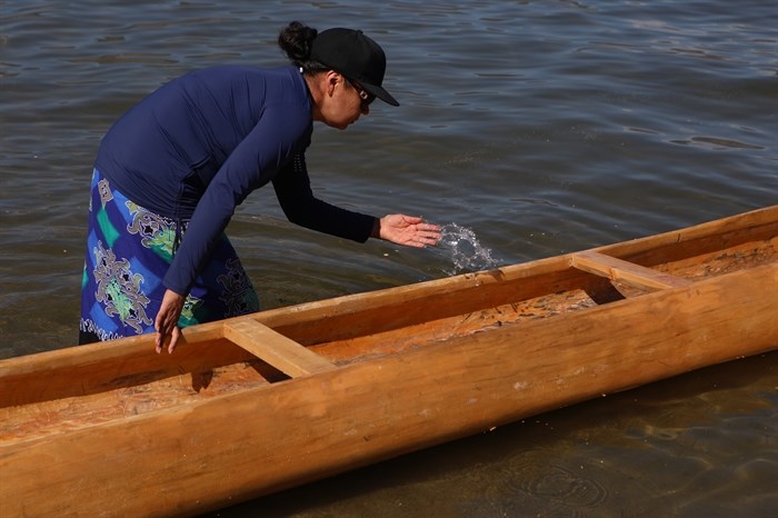 A community member splashes water into a canoe prior to the launch of the 2024 Suk?naqin canoe journey. Photo by 