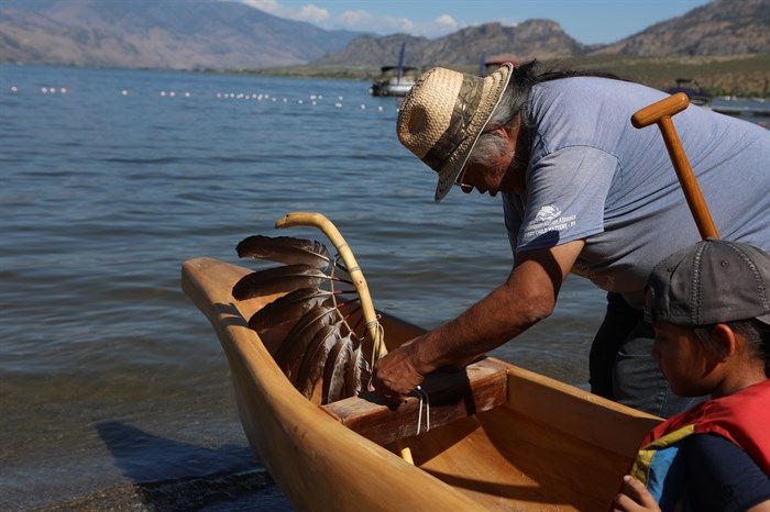 Herman Edward ties an eagle staff to the head of a canoe, prior to the launch of the 2024 Suk?naqin canoe journey. Photo by 