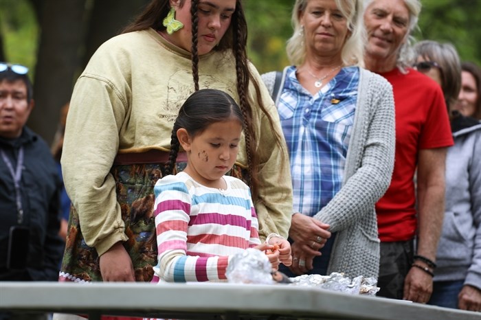Community members line up and take pieces of salmon during the syilx Nation’s 2024 salmon feast and celebration at sx???x??nitk? (Okanagan Falls) on Sept. 22.