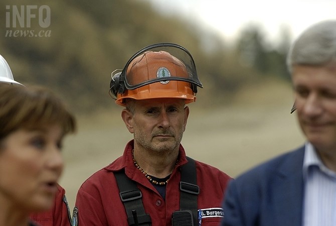 A firefighter stands behind the Prime Minister and Premier Christy Clark during a staged photo op in West Kelowna last week. The story has made national headlines for refusing to name the Prime Minister.