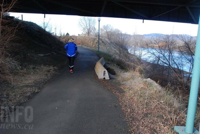 A jogger under the Yellowhead Bridge jogs past barricades blocking off the river banks erosion.