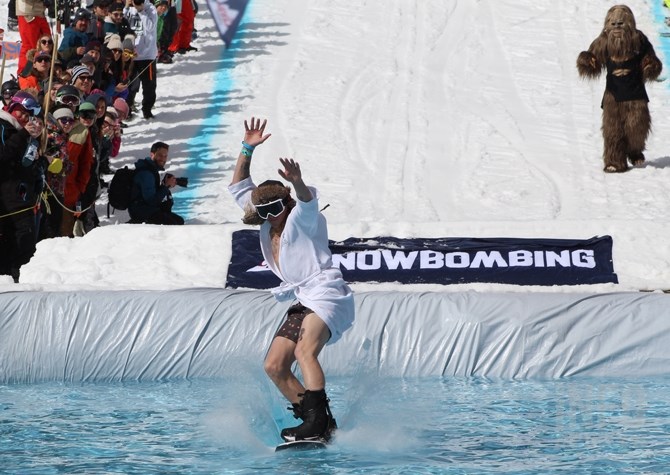 A sasquatch watches a man in a house coat snowboard into a pool of water as part of Snowbombing 2017.