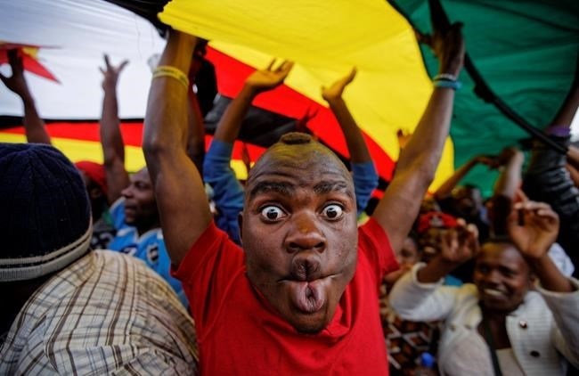 A happy protester pulls a face as he and others stand under a large national flag, at a demonstration of tens of thousands at Zimbabwe Grounds in Harare, Zimbabwe Saturday, Nov. 18, 2017.