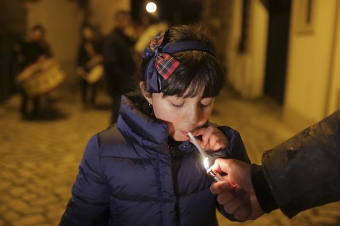 An adult helps a young girl light a cigarette as a band plays in the background in the village of Vale de Salgueiro, northern Portugal, during the local Kings’ Feast Friday, Jan. 5, 2018.