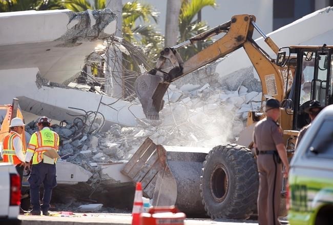 Workers use a backhoe on a section of a collapsed pedestrian bridge, Friday, March 16, 2018 near Florida International University in the Miami area.