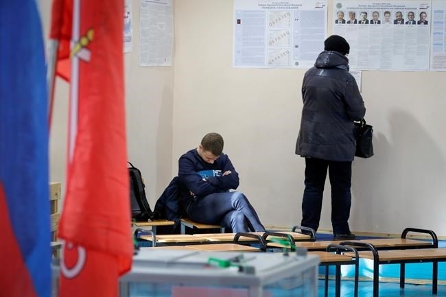 A woman examines a poster of candidates as an observer sleeps at a polling station during presidential elections in St.Petersburg, Russia, Sunday, March 18, 2018.