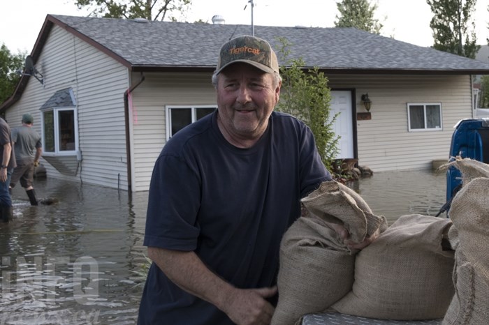Bill Pierce grabs a sandbag. Behind him the neighbours house stands submerged in water. 