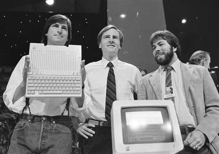 FILE PHOTO - In this April 24, 1984 file photo, Steve Jobs, left, chairman of Apple Computers, John Sculley, center, president and CEO, and Steve Wozniak, co-founder of Apple, unveil the new Apple IIc computer in San Francisco, Calif. Apple has become the world’s first company to be valued at $1 trillion, the financial fruit of tasteful technology that has redefined society since two mavericks named Steve started the company 42 years ago.