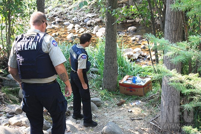 Bylaw officer Glenn Duffield and Darren Calibaba seize a box of food left beside Penticton Creek. Nearby the officers also found a discarded debit card.