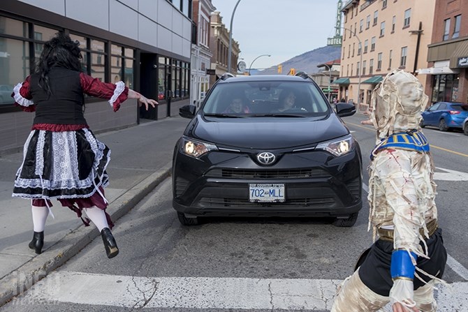 Two people in a car are surrounded by zombies crossing the street.