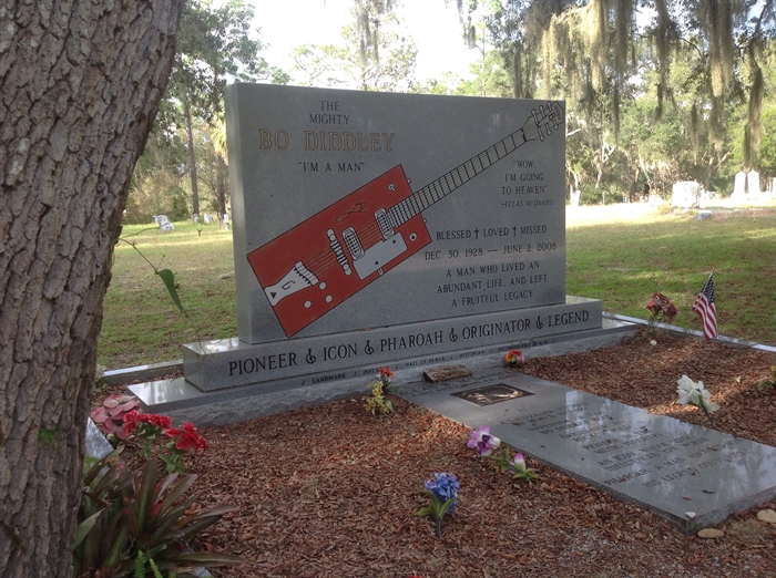 Bo Diddley's classic Gretchen red electric guitar, and his adopted name, Ella's B. McDaniel on his headstone in Bronson, FL.