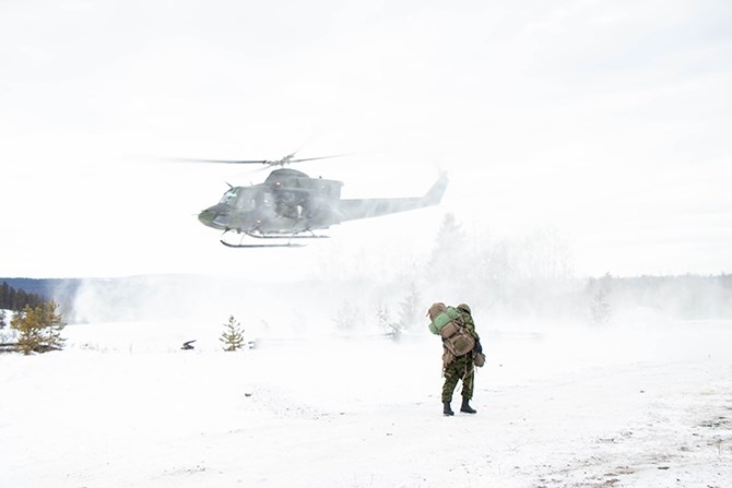 The helicopter creates formidable winds as it lifts off from the ground. It is not snowing but the force from the blades kicks up snow and blows it for several meters as a soldier walks towards the landing zone.