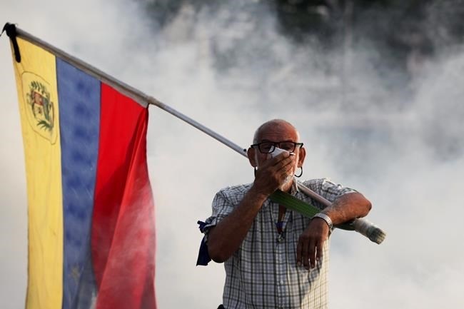 An opponent to Venezuelan President Nicolas Maduro carrying a Venezuelan flag covers his face amid tear gas fired by soldiers loyal to Maduro during an attempted military uprising in Caracas, Venezuela, Tuesday, April 30, 2019. Venezuelan opposition leader Juan GuaidÃ³ and jailed opposition leader Leopoldo Lopez took to the streets with a small contingent of armed troops early Tuesday in a call for the military to rise up and oust Maduro.