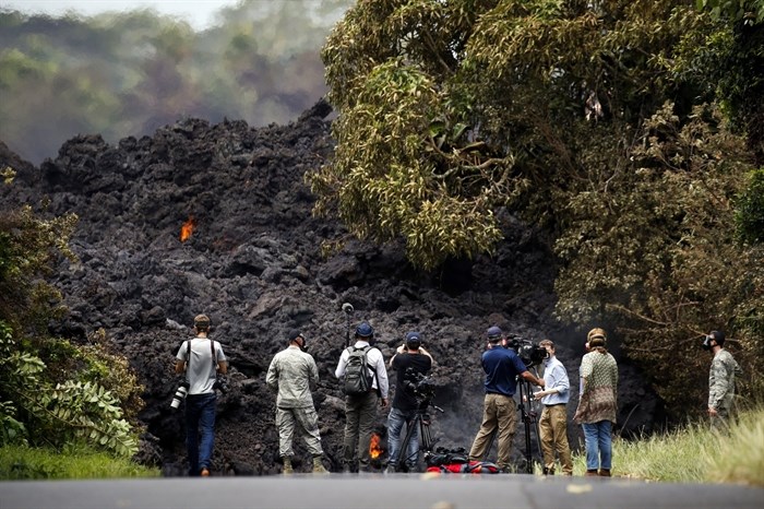 FILE - In this May 20, 2018 file photo, members of the media record a wall of lava entering the ocean near Pahoa, Hawaii. It’s been a year since a Hawaii volcano rained lava and gases on a rural swath of the Big Island in one of its largest and most destructive eruptions in recorded history. More than 700 homes were destroyed in the historic eruption, which started May 3 and buried an area more than half the size of Manhattan in now-hardened rock.