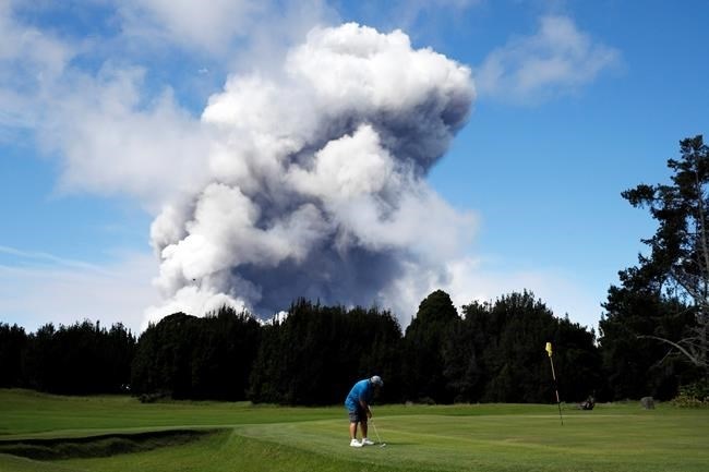 FILE - In this May 21, 2018 file photo, Doug Ralston plays golf in Volcano, Hawaii, as a huge ash plume rises from the summit of Kiluaea volcano. A year after the Hawaii volcano rained lava and gases on a rural swath of the Big Island in one of its largest and most destructive eruptions in recorded history, people who lost their homes and farms in the disaster are still struggling to return to their island lifestyle.