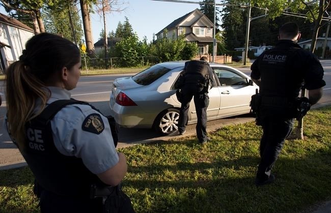 Members of the RCMP Gang Enforcement Team is silhouetted as he speaks to the occupants of a car during a stop in Surrey, B.C., Friday, May 31, 2019.