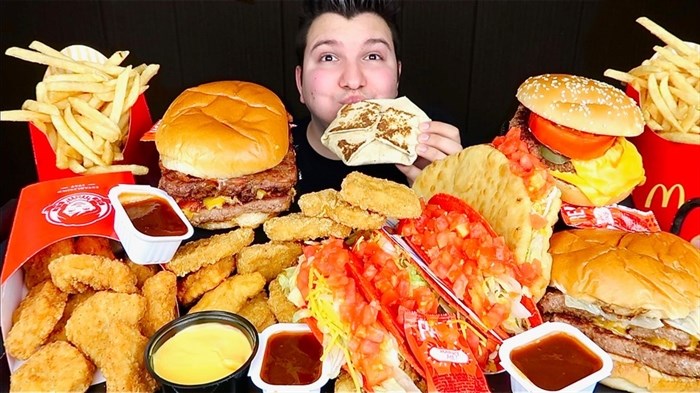 This image taken from video and released by Nikocado Avocado shows him surrounded by items from fast-food chains Wendy's and Taco Bell. Nikocado Avocado, whose real name is Nicholas Perry, 27, has three mukbang channels with 1.71 million subscribers on the largest. He’s a classically trained violinist who gave up that career struggle for mukbang in 2016. 