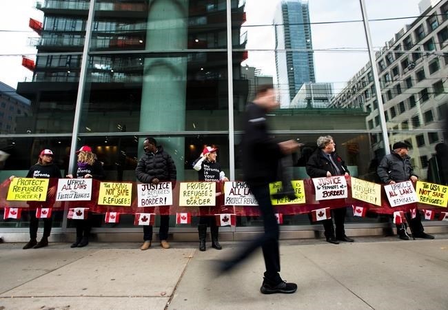 Protesters stand outside the Federal Court of Canada building for a hearing of the designation of the U.S. as a safe third country for refugees in Toronto on Monday, November 4, 2019. 
