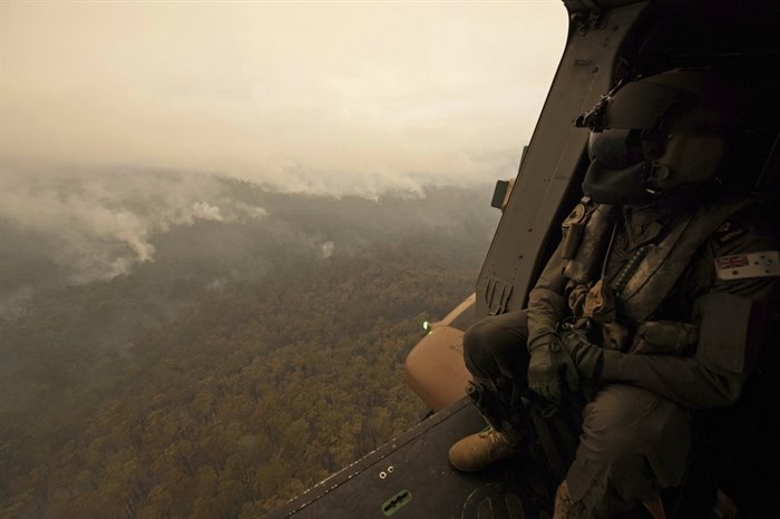 In this Sunday, Jan. 5, 2020, photo provided by Australian Department of Defence, a Royal Australian Navy MRH-90 helicopter crew member looks out over fires burning near Cann River, Australia. The wildfires have so far scorched an area twice the size of the U.S. state of Maryland. 