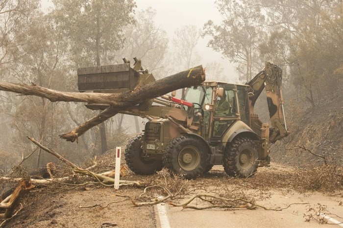 In this image released and dated on Jan. 6, 2020, from Australian Department of Defence, plant operators Cpl. Duncan Keith and Sapper Ian Larner of the 22nd Engineer Regiment use a 434 backhoe to assist staff from Forestry Management Victoria to clear fire damaged trees from the great Alpine road between Bairnsdale and Omeo during Operation Bushfire Assist 19-20 in Bairnsdale, Victoria, Australia. Australia's government on Monday said it was willing to pay “whatever it takes” to help communities recover from deadly wildfires that have ravaged the country.