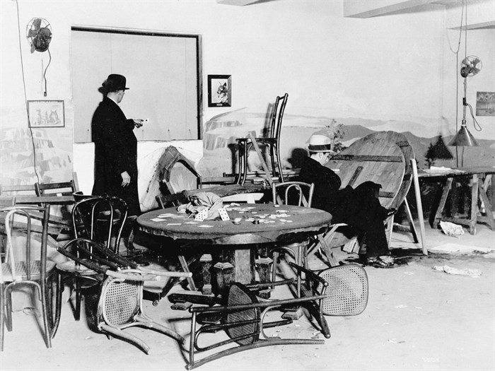 FILE - In this Dec. 31, 1931, file photo the wrecked speakeasy in the Hotel Victoria in mid-Manhattan, where Louis Levine, alias Louis Taylor, a small-time gambler, was killed by one of three gunmen earlier in the day in New York. A bystander points to a bullet hole in the wall, while another is seated in the chair where Levine, known as 