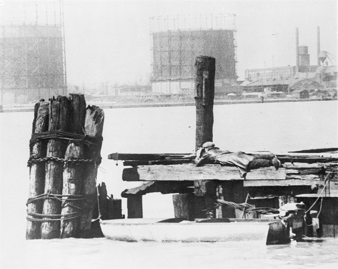 FILE - In this April 28, 1929, file photo a rum runner in Windsor, on the Canadian side of the Detroit River, watches with field glasses for lookout on the American side to signal that no prohibition agents are in sight. His outboard motorboat, loaded with illegal liquor, is shown beneath pilings. 