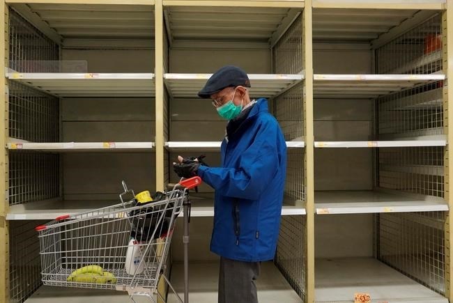 A man wearing face mask stands near an empty shelf of rice at a supermarket in Hong Kong, Thursday, Feb. 6, 2020. 