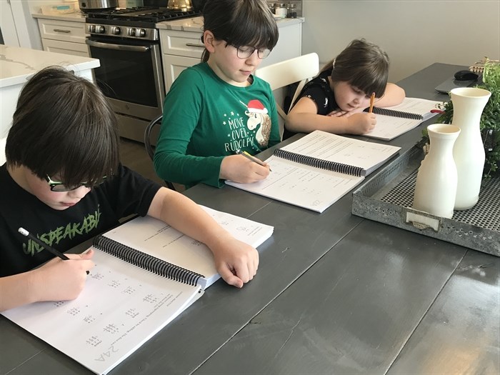 From left: Ethan, 8, Lauren, 10, and Izzy, 6, work on the day's lesson at the kitchen table.