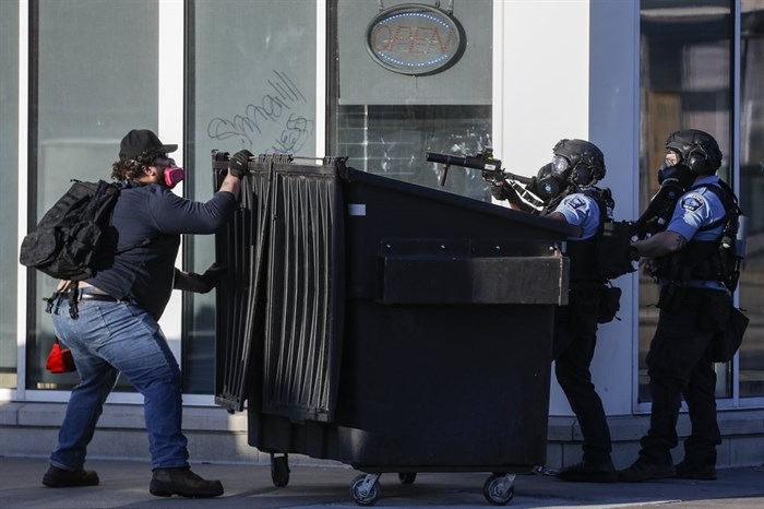 A protestor faces off with two police officers using less-lethal ammunition in their weapons, Thursday, May 28, 2020, in St. Paul, Minn. Protests over the death of George Floyd, a black man who died in police custody Monday, broke out in Minneapolis for a third straight night. 